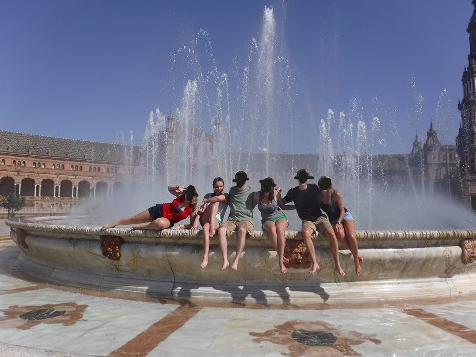 Six young adults sit on a fountain in Seville, Spain