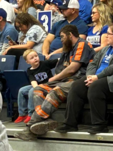 A man sits with his son watching a game, but the dad is still dirty from working the mines that same day